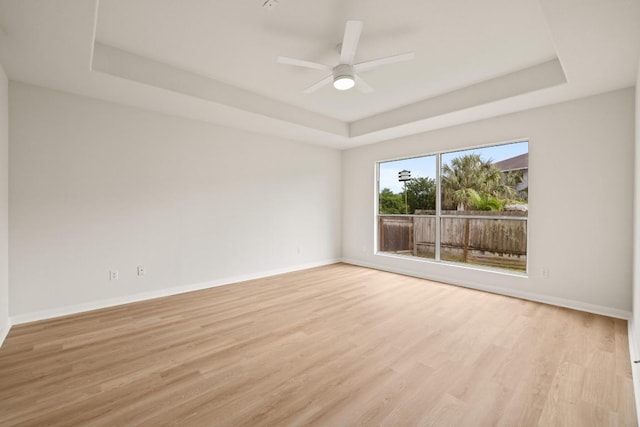 spare room featuring a tray ceiling, light wood-style flooring, baseboards, and a ceiling fan