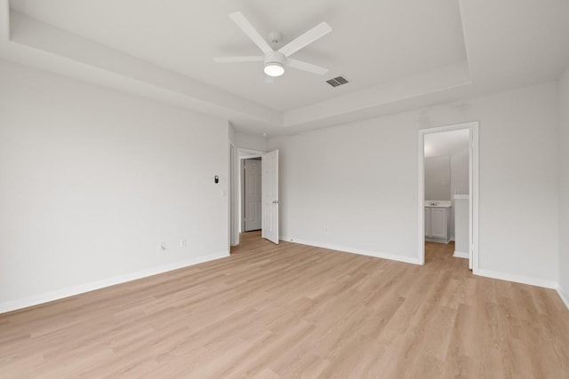 unfurnished bedroom featuring a tray ceiling, light wood-type flooring, baseboards, and connected bathroom