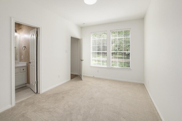 unfurnished bedroom with light carpet, ensuite bath, and baseboards