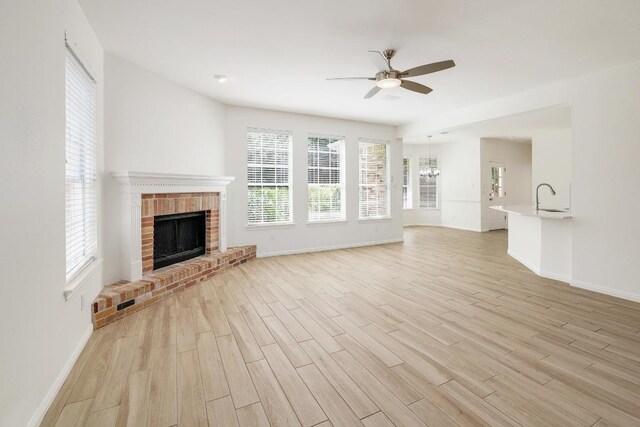 unfurnished living room featuring ceiling fan, a sink, a fireplace, light wood finished floors, and baseboards