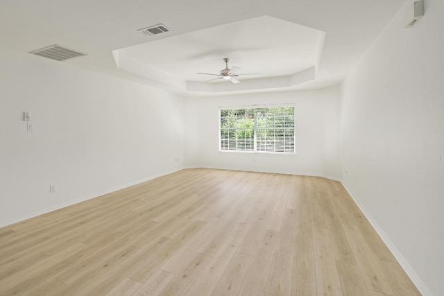 spare room featuring a tray ceiling, light wood finished floors, a ceiling fan, and baseboards