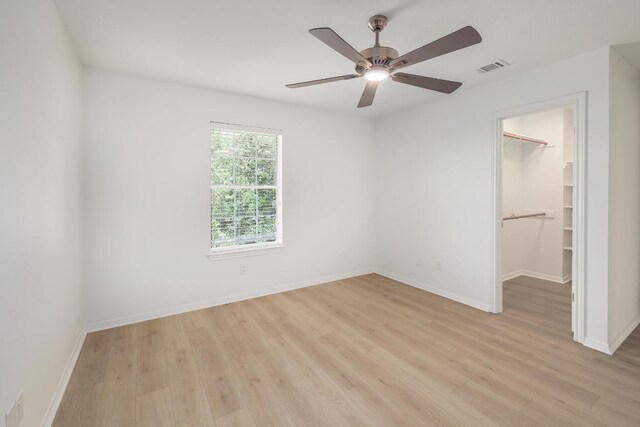 unfurnished bedroom featuring light wood finished floors, a walk in closet, baseboards, a closet, and a ceiling fan