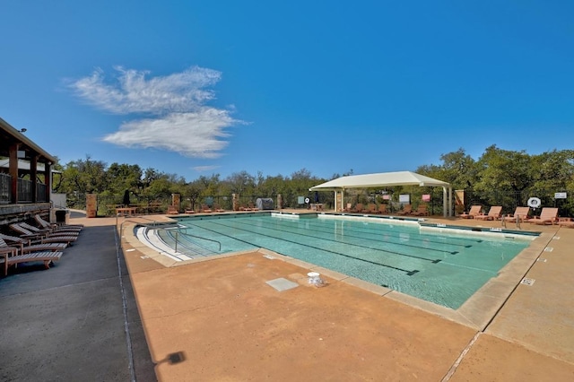 community pool featuring a patio area, fence, and view of wooded area