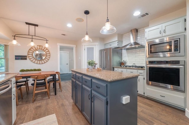 10305 Pickfair Dr, Austin, TX 78750 - kitchen with appliances with stainless steel finishes, wall chimney exhaust hood, tasteful backsplash, wood finished floors, and a center island