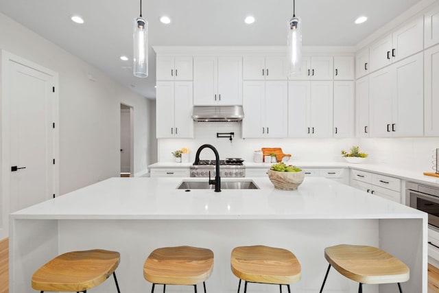 kitchen featuring under cabinet range hood, a sink, recessed lighting, backsplash, and light countertops