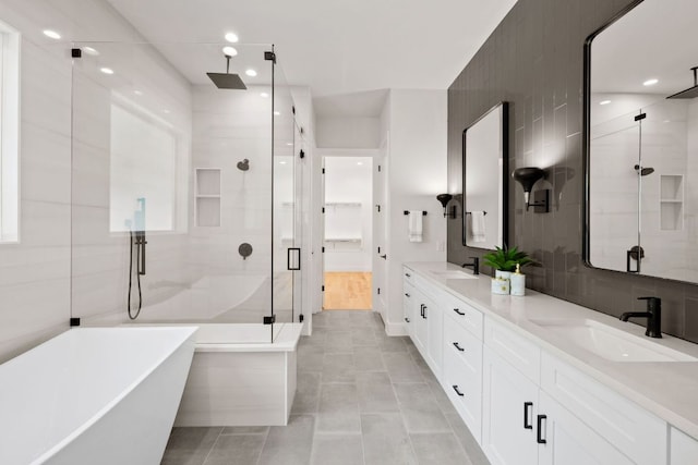 bathroom with a shower stall, double vanity, a freestanding tub, tile walls, and tile patterned flooring