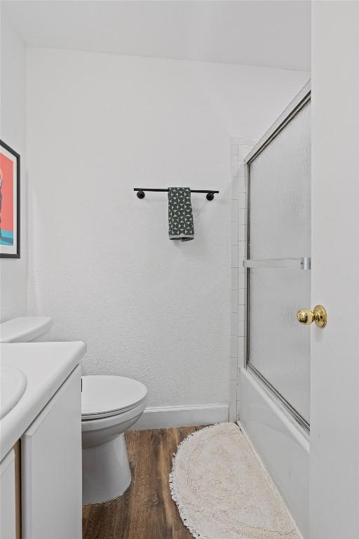 bathroom featuring wood finished floors, vanity, enclosed tub / shower combo, toilet, and baseboards