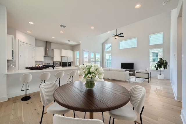 dining space featuring plenty of natural light, a ceiling fan, light wood-style floors, recessed lighting, and a towering ceiling