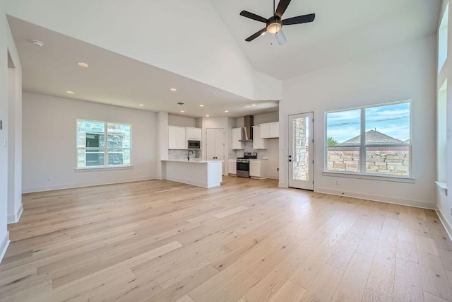 unfurnished living room with light wood-type flooring, ceiling fan, high vaulted ceiling, recessed lighting, and baseboards