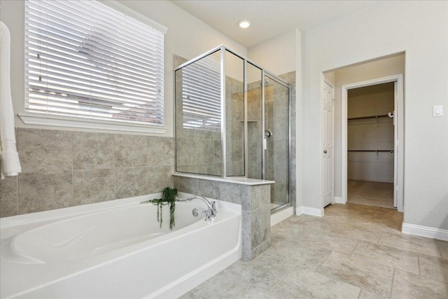bathroom featuring a shower stall, a garden tub, a walk in closet, and baseboards