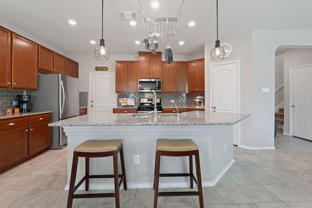 kitchen with appliances with stainless steel finishes, tasteful backsplash, a breakfast bar area, brown cabinets, and recessed lighting