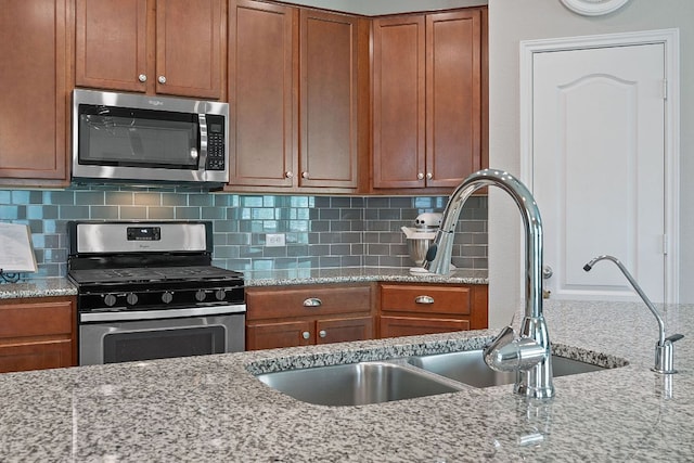kitchen featuring stainless steel appliances, decorative backsplash, brown cabinetry, and light stone countertops