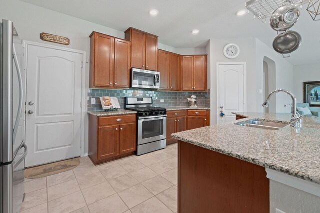 kitchen with stainless steel appliances, a sink, decorative backsplash, light stone countertops, and brown cabinets
