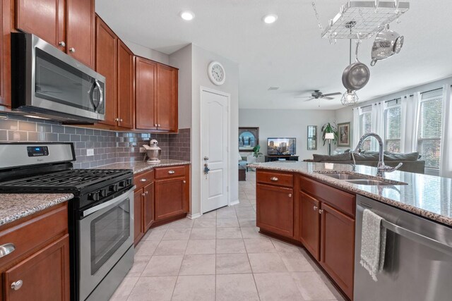 kitchen featuring appliances with stainless steel finishes, a sink, decorative backsplash, open floor plan, and brown cabinetry