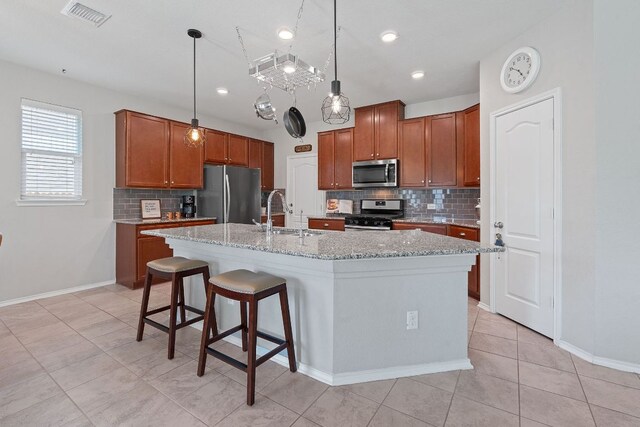 kitchen featuring appliances with stainless steel finishes, a sink, decorative backsplash, an island with sink, and brown cabinets
