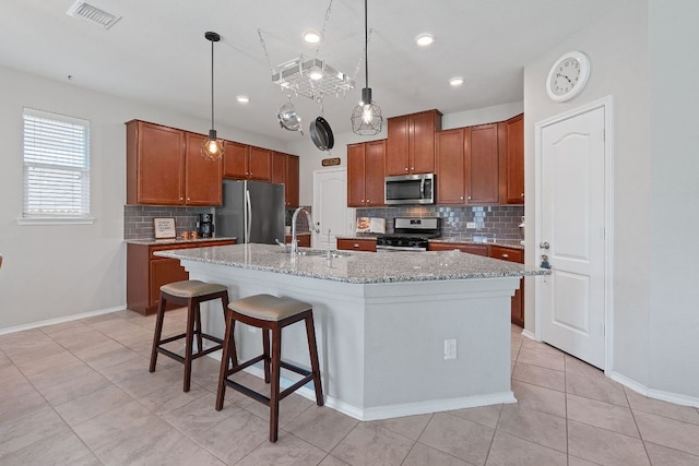 476 Sheepshank Dr, Georgetown, TX 78633 - kitchen featuring appliances with stainless steel finishes, tasteful backsplash, a kitchen island with sink, and brown cabinetry