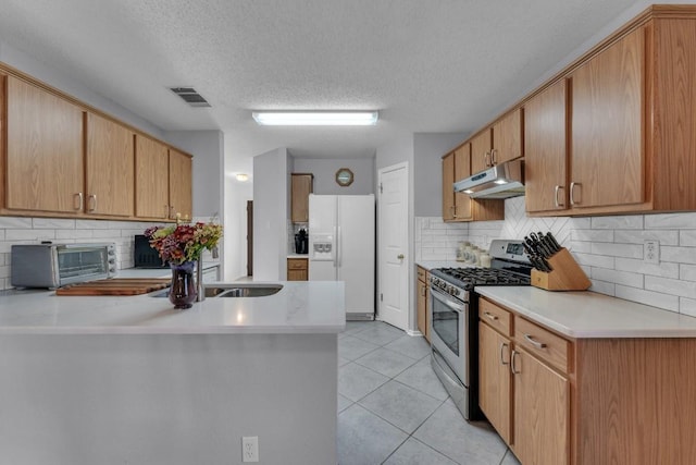 302 Debora Dr, Georgetown, TX 78628 - kitchen featuring stainless steel gas stove, white refrigerator with ice dispenser, under cabinet range hood, a peninsula, and light countertops