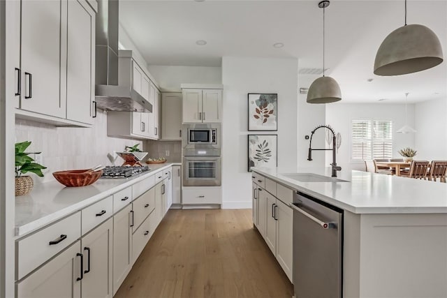 1809 Pasadena Dr, Austin, TX 78757 - kitchen featuring stainless steel appliances, a sink, wall chimney exhaust hood, light countertops, and light wood-type flooring