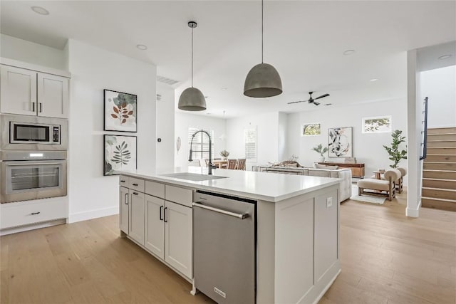 1809 Pasadena Dr, Austin, TX 78757 - kitchen featuring appliances with stainless steel finishes, light wood-type flooring, light countertops, a kitchen island with sink, and hanging light fixtures