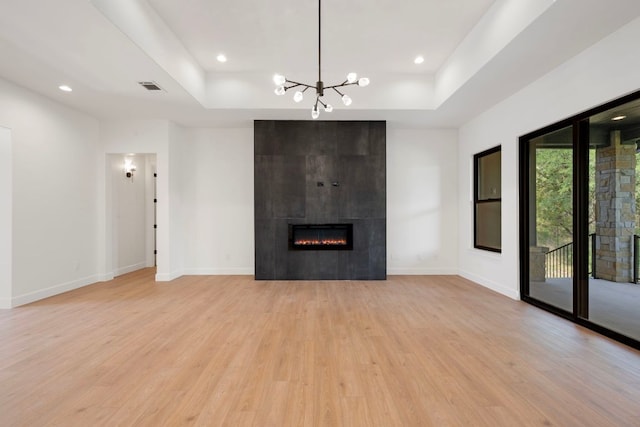 310 Apache Tears, Horseshoe Bay, TX 78657 - unfurnished living room with a raised ceiling, light wood-type flooring, a tiled fireplace, a chandelier, and recessed lighting