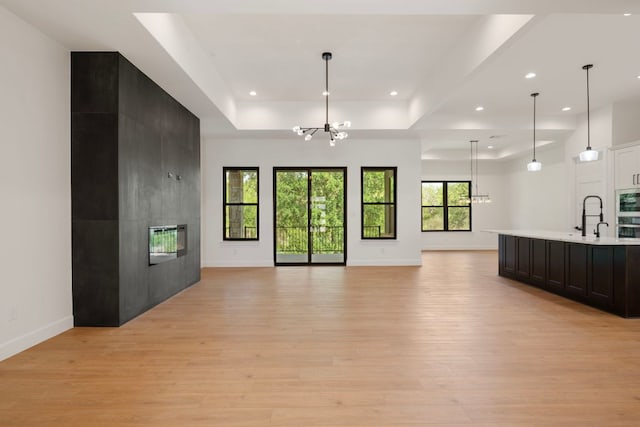 310 Apache Tears, Horseshoe Bay, TX 78657 - unfurnished living room with a chandelier, light wood finished floors, a raised ceiling, baseboards, and a tile fireplace