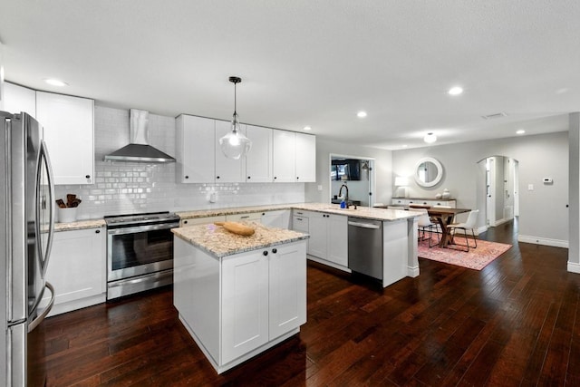 701 Nixon St, Lockhart, TX 78644 - kitchen with wall chimney range hood, appliances with stainless steel finishes, a peninsula, arched walkways, and a kitchen island