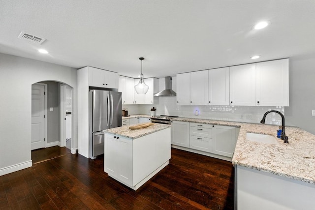 701 Nixon St, Lockhart, TX 78644 - kitchen with appliances with stainless steel finishes, wall chimney exhaust hood, a sink, arched walkways, and light stone countertops