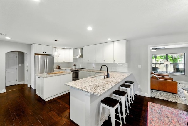 701 Nixon St, Lockhart, TX 78644 - kitchen with appliances with stainless steel finishes, wall chimney exhaust hood, a sink, arched walkways, and dark wood-style floors