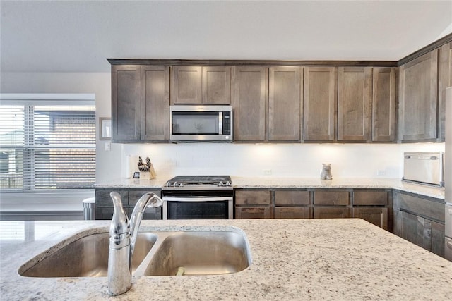 131 Mount Ellen St, Hutto, TX 78634 - kitchen featuring stainless steel appliances, a sink, dark brown cabinets, light stone countertops, and backsplash