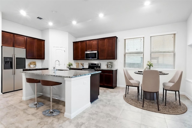 19201 Quebrada Dr, Pflugerville, TX 78660 - kitchen with appliances with stainless steel finishes, an island with sink, a breakfast bar, light stone countertops, and recessed lighting