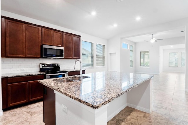 19201 Quebrada Dr, Pflugerville, TX 78660 - kitchen featuring appliances with stainless steel finishes, tasteful backsplash, light stone counters, a kitchen island with sink, and ceiling fan