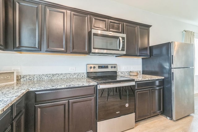 533 Peony Ct, Jarrell, TX 76537 - kitchen with appliances with stainless steel finishes, dark brown cabinets, light stone countertops, and light wood-style flooring