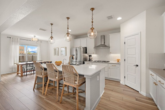 kitchen with wall chimney range hood, stainless steel refrigerator with ice dispenser, a center island with sink, a kitchen breakfast bar, and tasteful backsplash