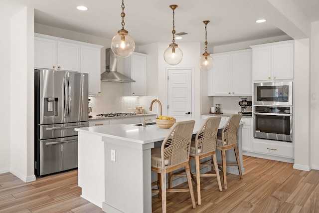 kitchen with stainless steel appliances, wall chimney range hood, light wood-type flooring, tasteful backsplash, and recessed lighting