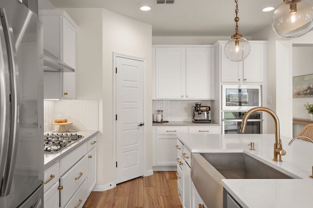 kitchen featuring appliances with stainless steel finishes, a sink, white cabinetry, under cabinet range hood, and light countertops