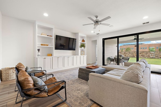 living area with wood finished floors, ceiling fan, recessed lighting, and built in shelves