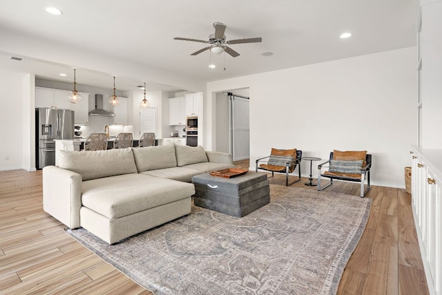 living area with ceiling fan, light wood-style flooring, recessed lighting, baseboards, and a barn door