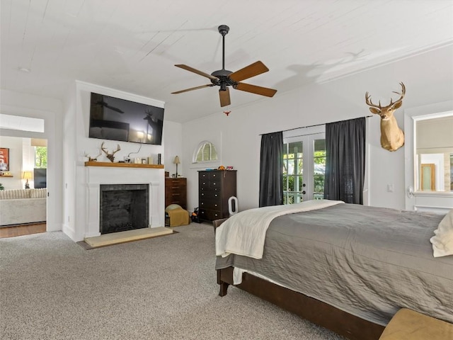 carpeted bedroom featuring french doors, a fireplace with raised hearth, and a ceiling fan