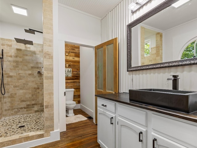 bathroom with wood finished floors, a tile shower, toilet, vanity, and crown molding