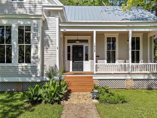 entrance to property with a standing seam roof, covered porch, metal roof, and a yard