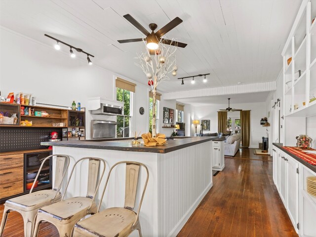 kitchen featuring dark countertops, ceiling fan, rail lighting, open floor plan, and dark wood-type flooring