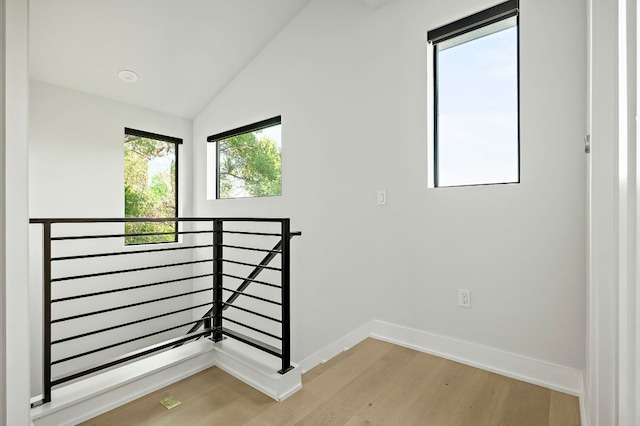 empty room featuring light wood-style flooring, baseboards, and lofted ceiling