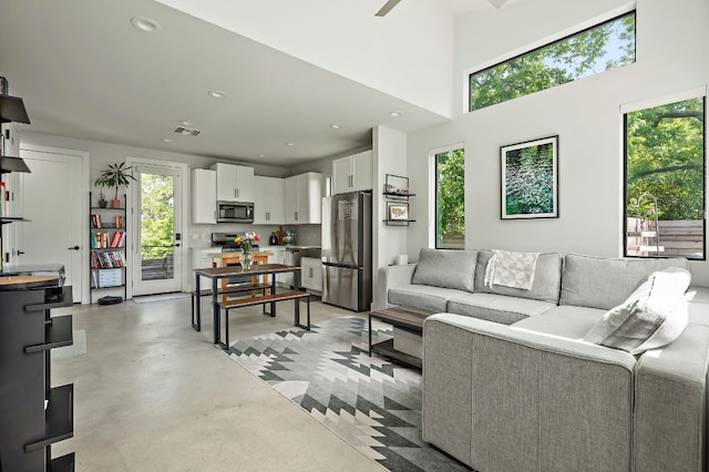 living area with plenty of natural light, finished concrete flooring, recessed lighting, a high ceiling, and ceiling fan