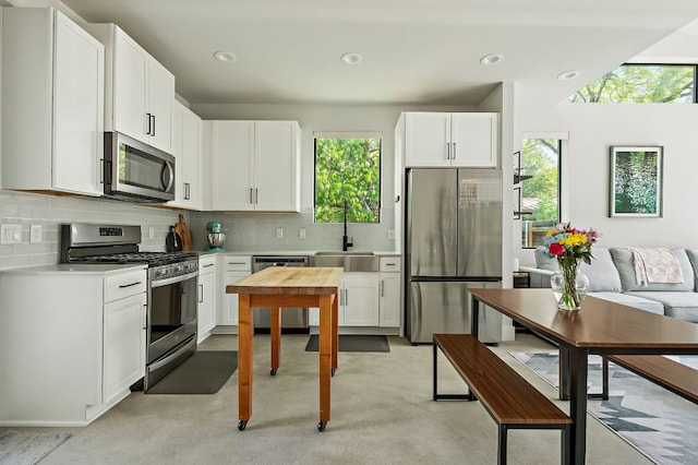kitchen with appliances with stainless steel finishes, a sink, light countertops, tasteful backsplash, and white cabinets