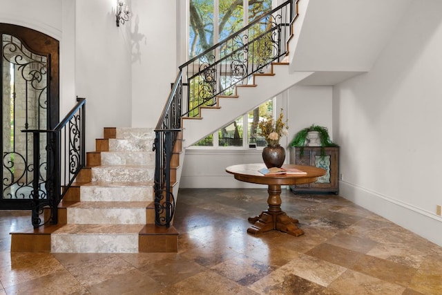 staircase with stone tile floors, arched walkways, baseboards, and a towering ceiling