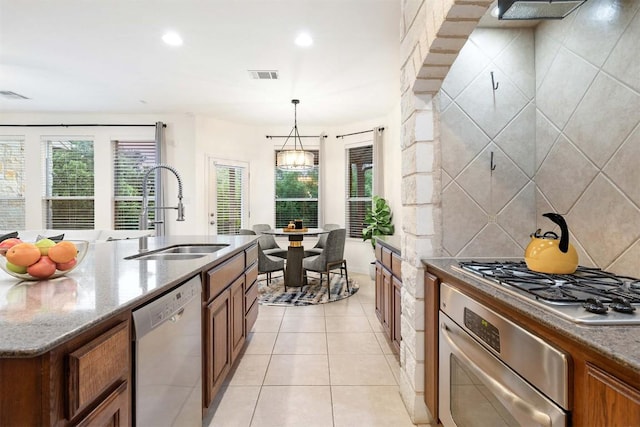 199 Limestone Trl, Austin, TX 78737 - kitchen featuring stainless steel appliances, brown cabinets, light tile patterned floors, stone counters, and hanging light fixtures