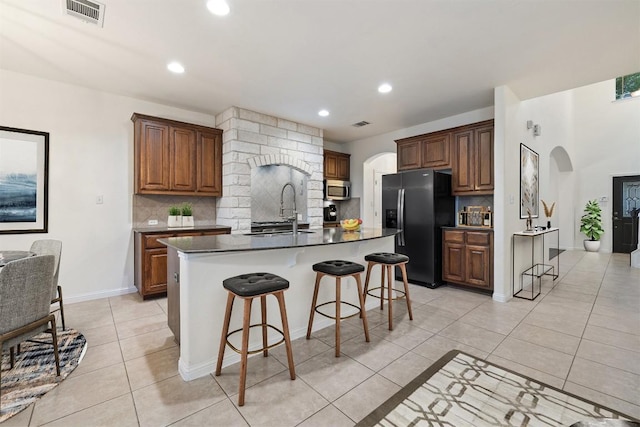 199 Limestone Trl, Austin, TX 78737 - kitchen featuring black refrigerator with ice dispenser, stainless steel microwave, arched walkways, decorative backsplash, and recessed lighting