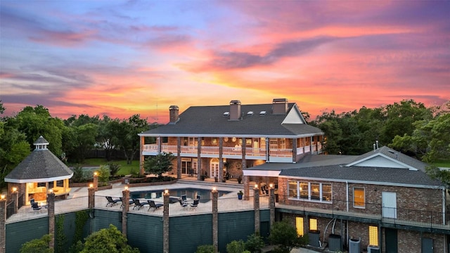 12 Hedge Ln, Austin, TX 78746 - back of property at dusk featuring a balcony, a chimney, a patio, and brick siding