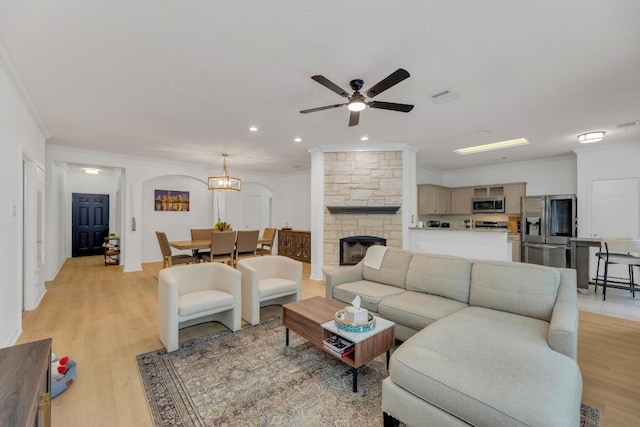 living area featuring ornamental molding, light wood finished floors, a ceiling fan, a stone fireplace, and recessed lighting
