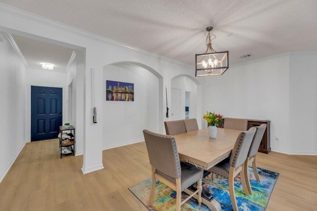 dining space with arched walkways, light wood finished floors, a chandelier, ornamental molding, and baseboards